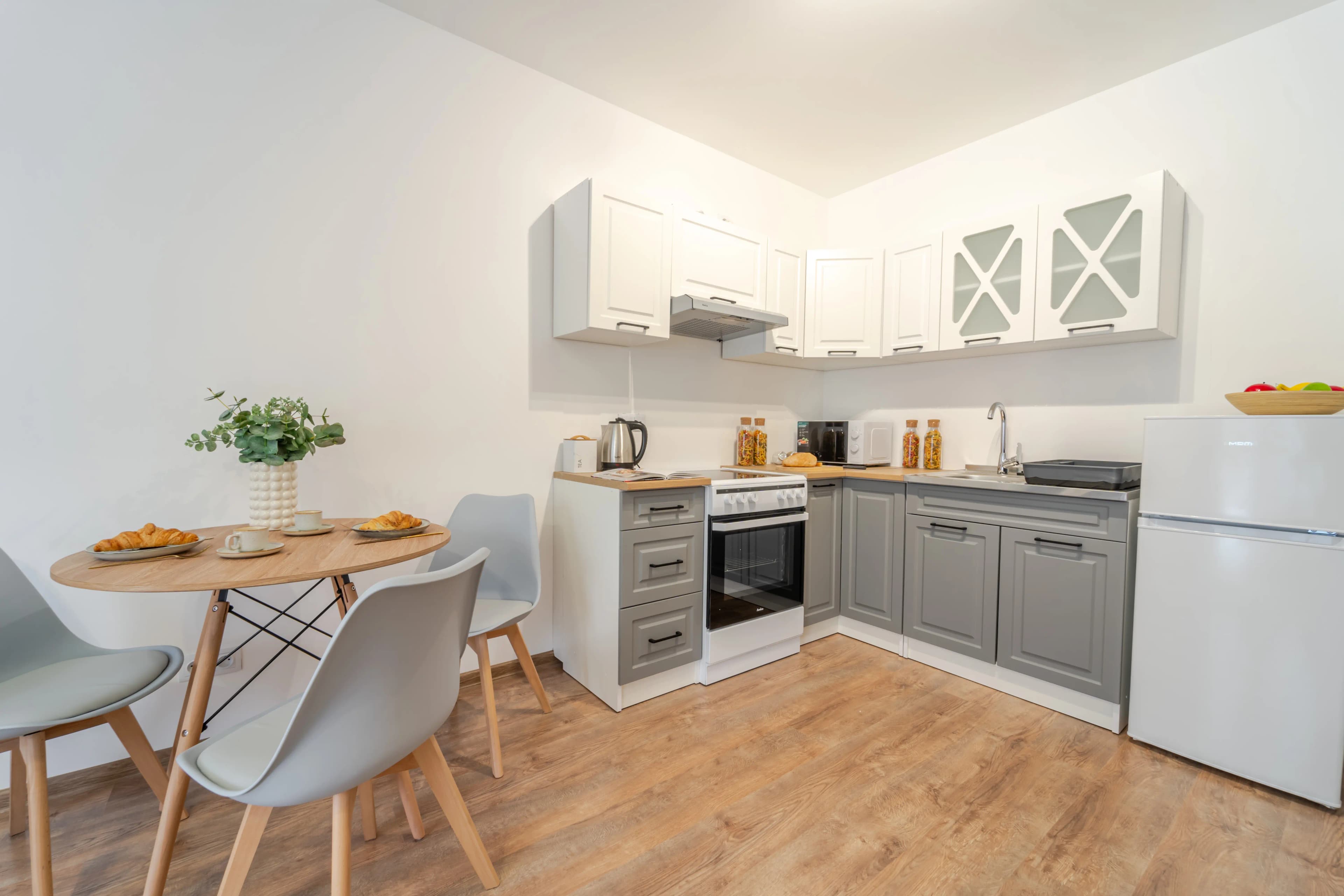 Funkcjonalny aneks kuchenny z szarymi frontami frezowanymi w stylu klasycznym, połączony z małą strefą jadalnianą.