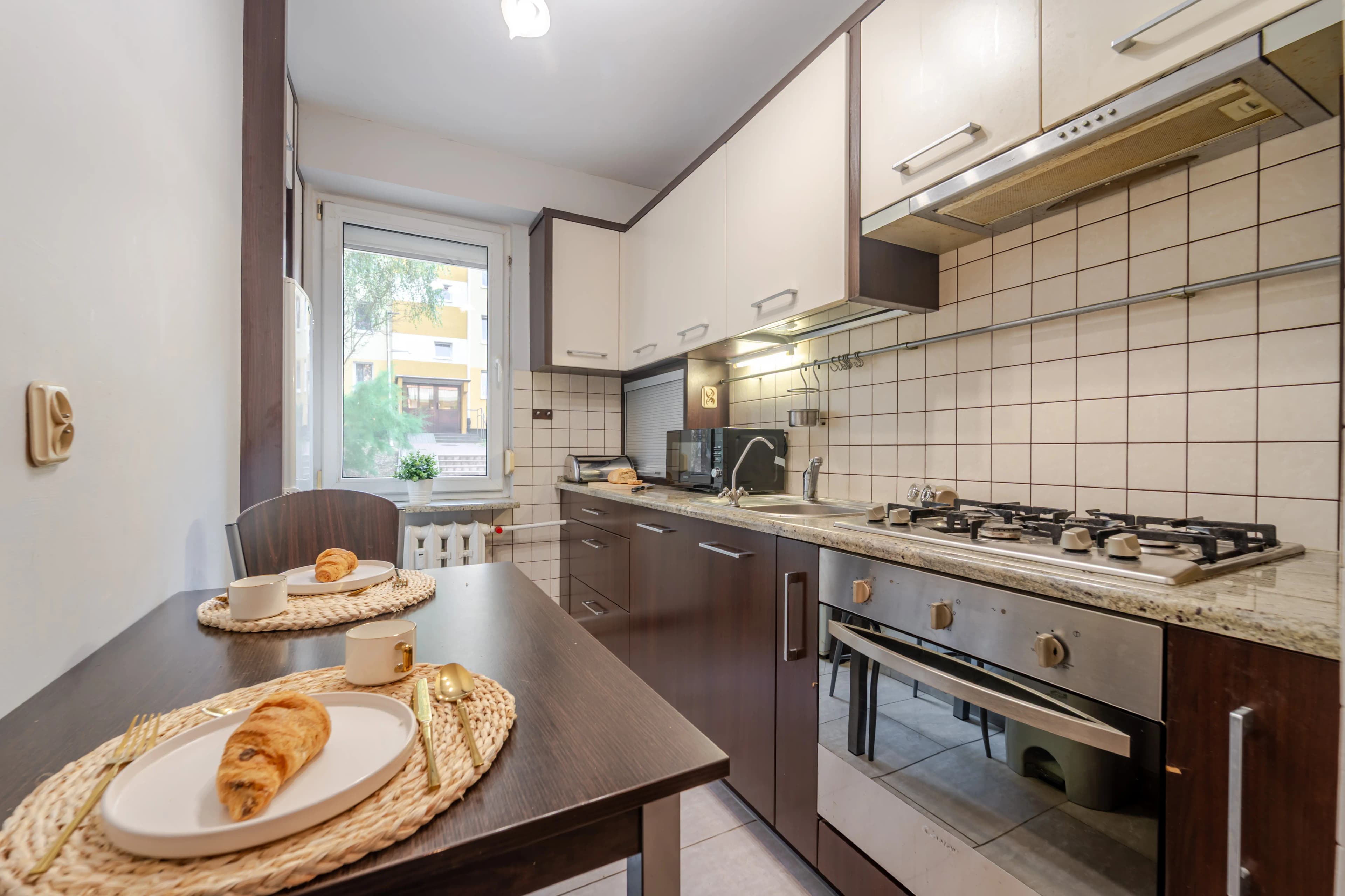 Tradycyjna kuchnia w brązach z ciemnym stołem śniadaniowym i ścianą wyłożoną jasnymi kafelkami.