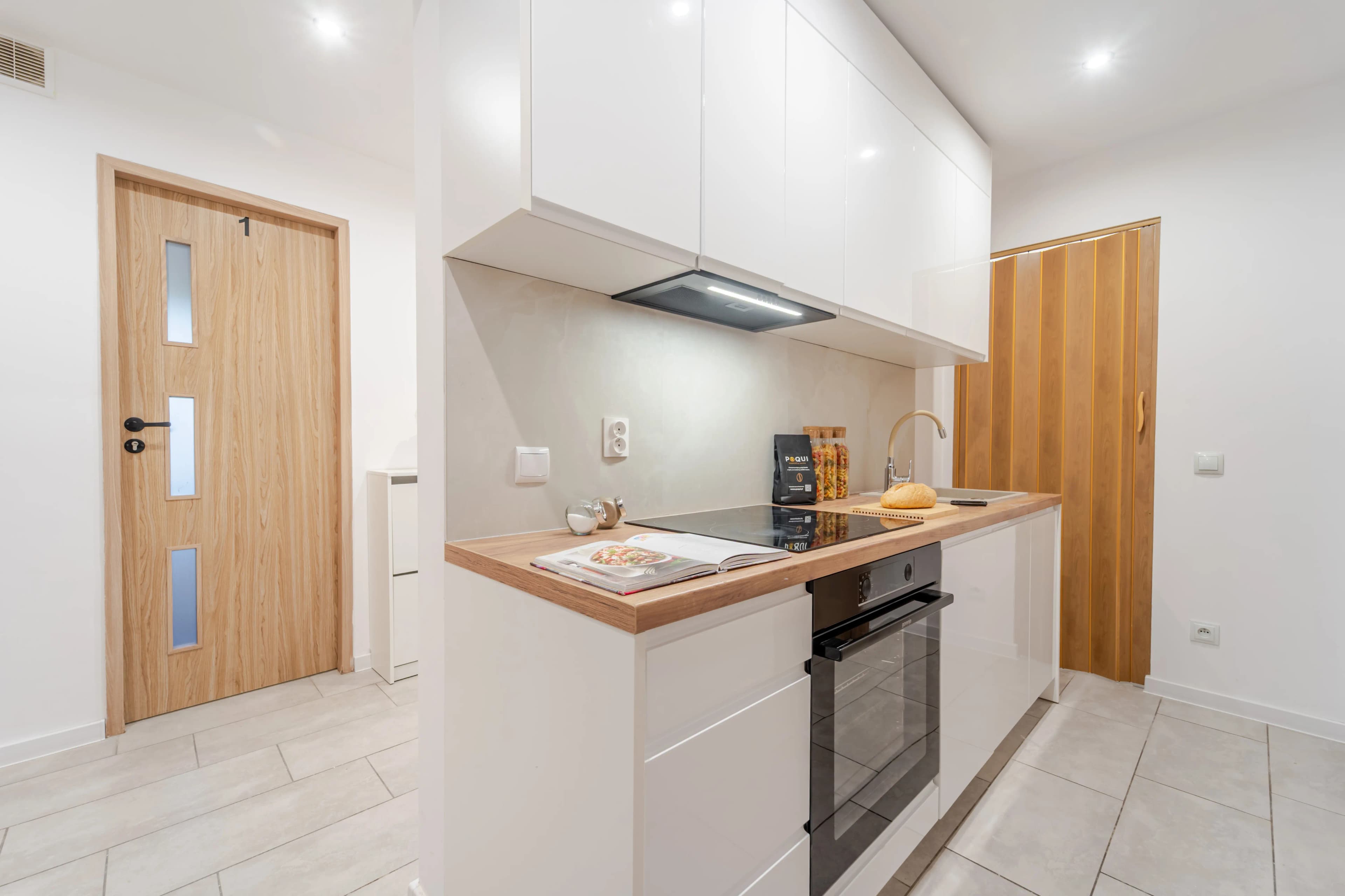 Kompaktowy aneks kuchenny w bieli z drewnianym blatem, usytuowany w strefie korytarza.