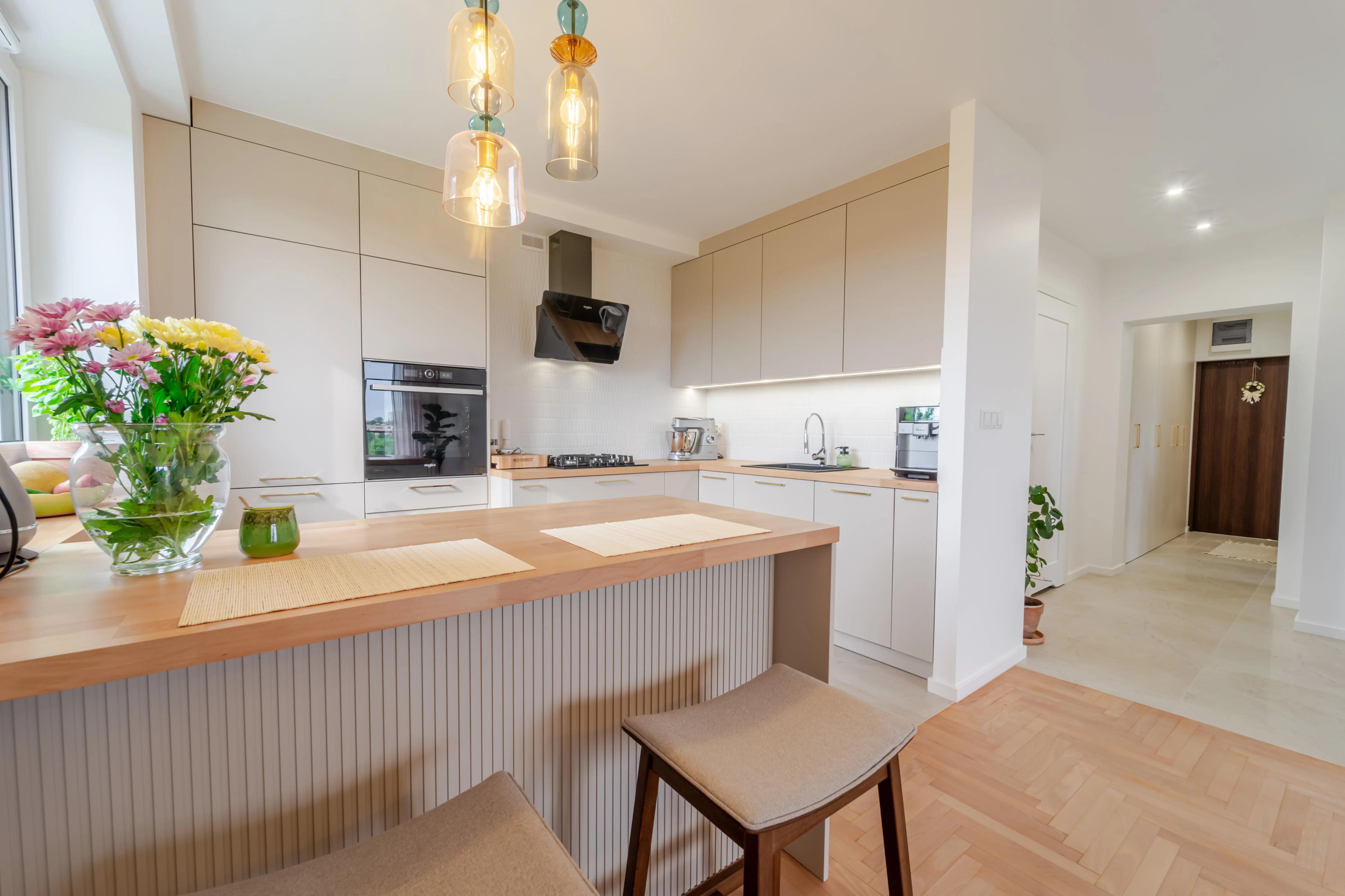 Beżowa kuchnia z ryflowaną wyspą, beżowymi hokeram.