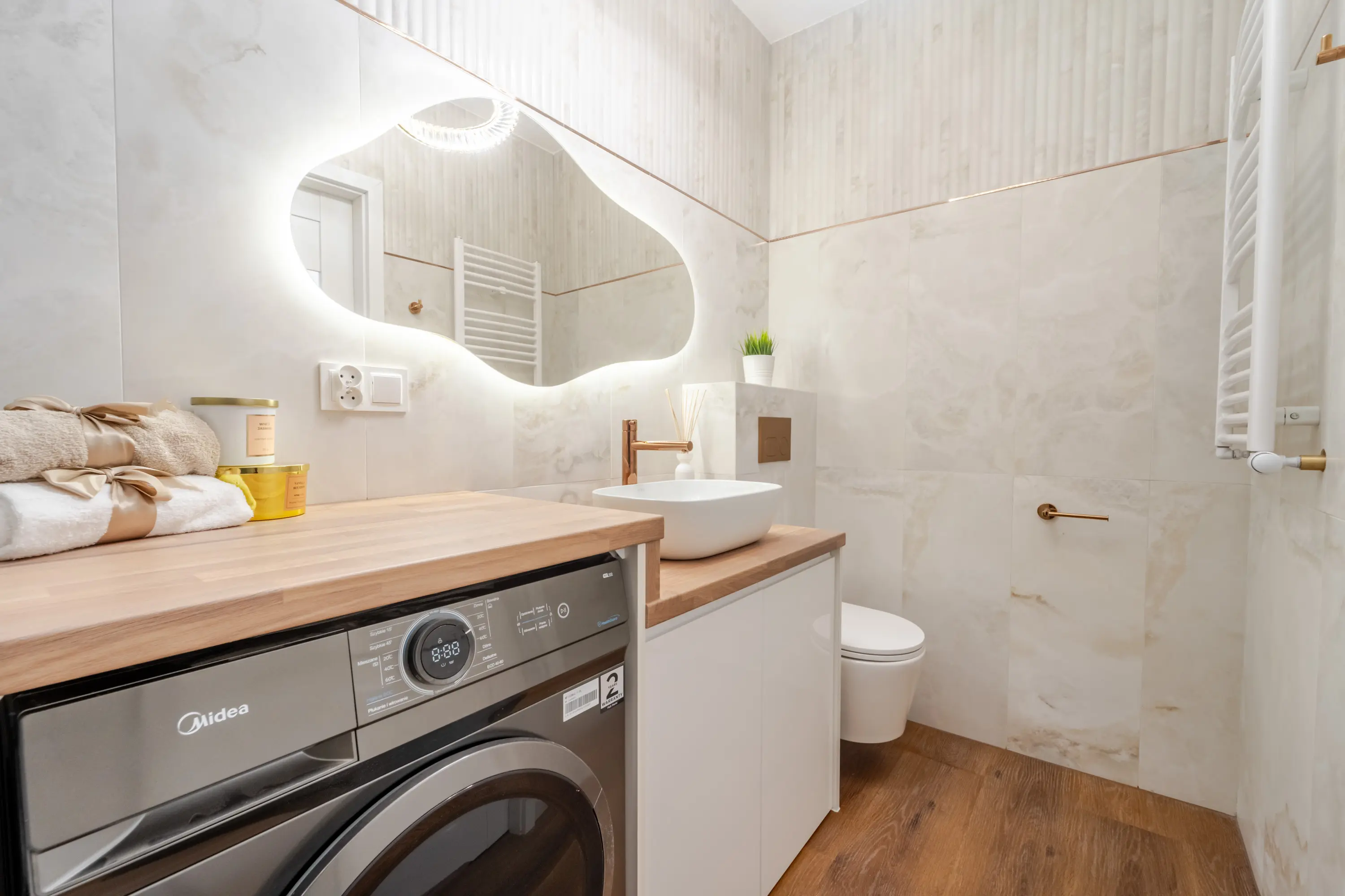 Nowoczesna łazienka z zabudowaną pralką pod blatem, chmurką lustrem LED i ryflowanymi płytkami na ścianie.