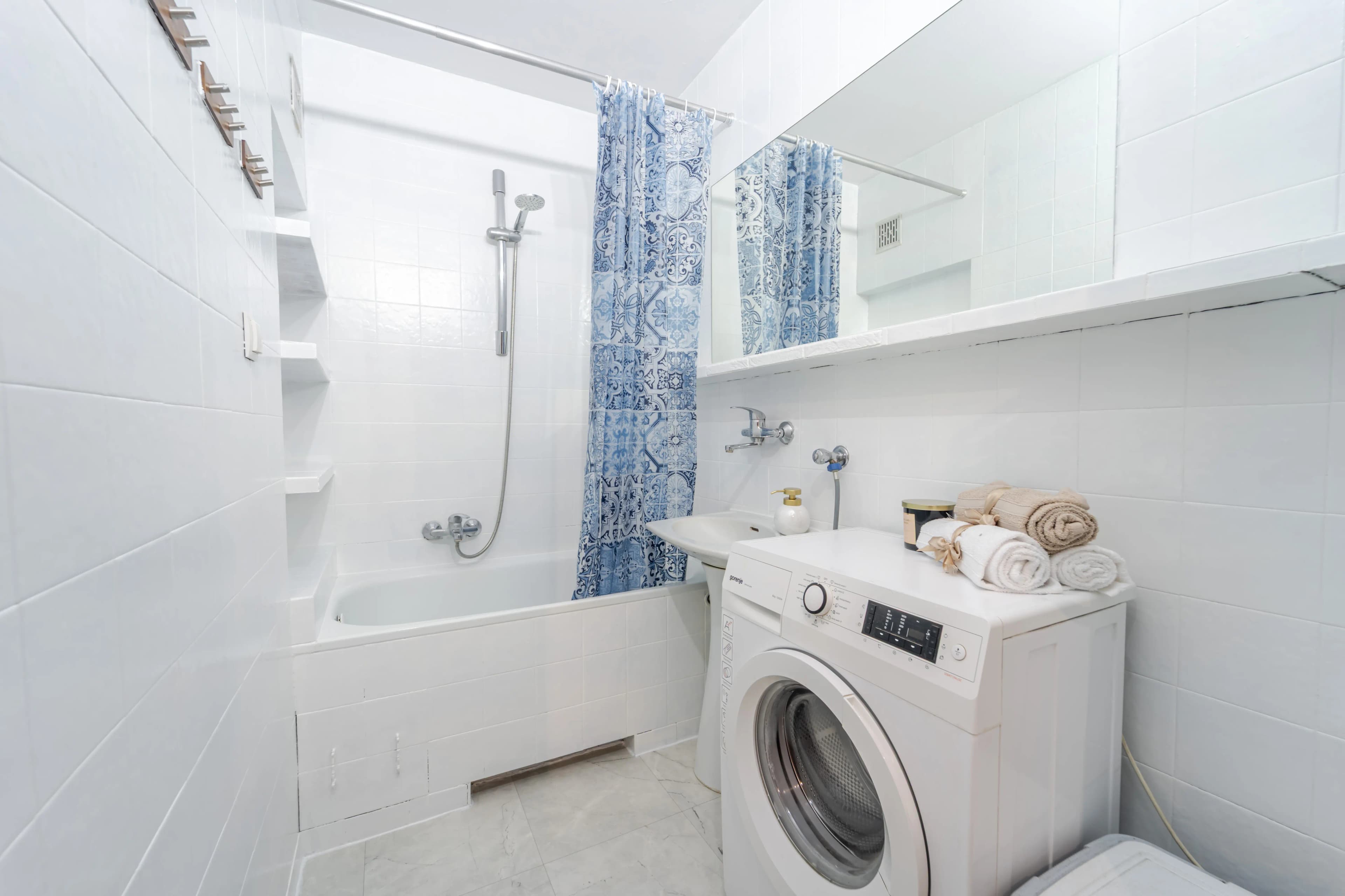 Funkcjonalna, biała łazienka z wanną, pralką i niebieską zasłoną prysznicową.
