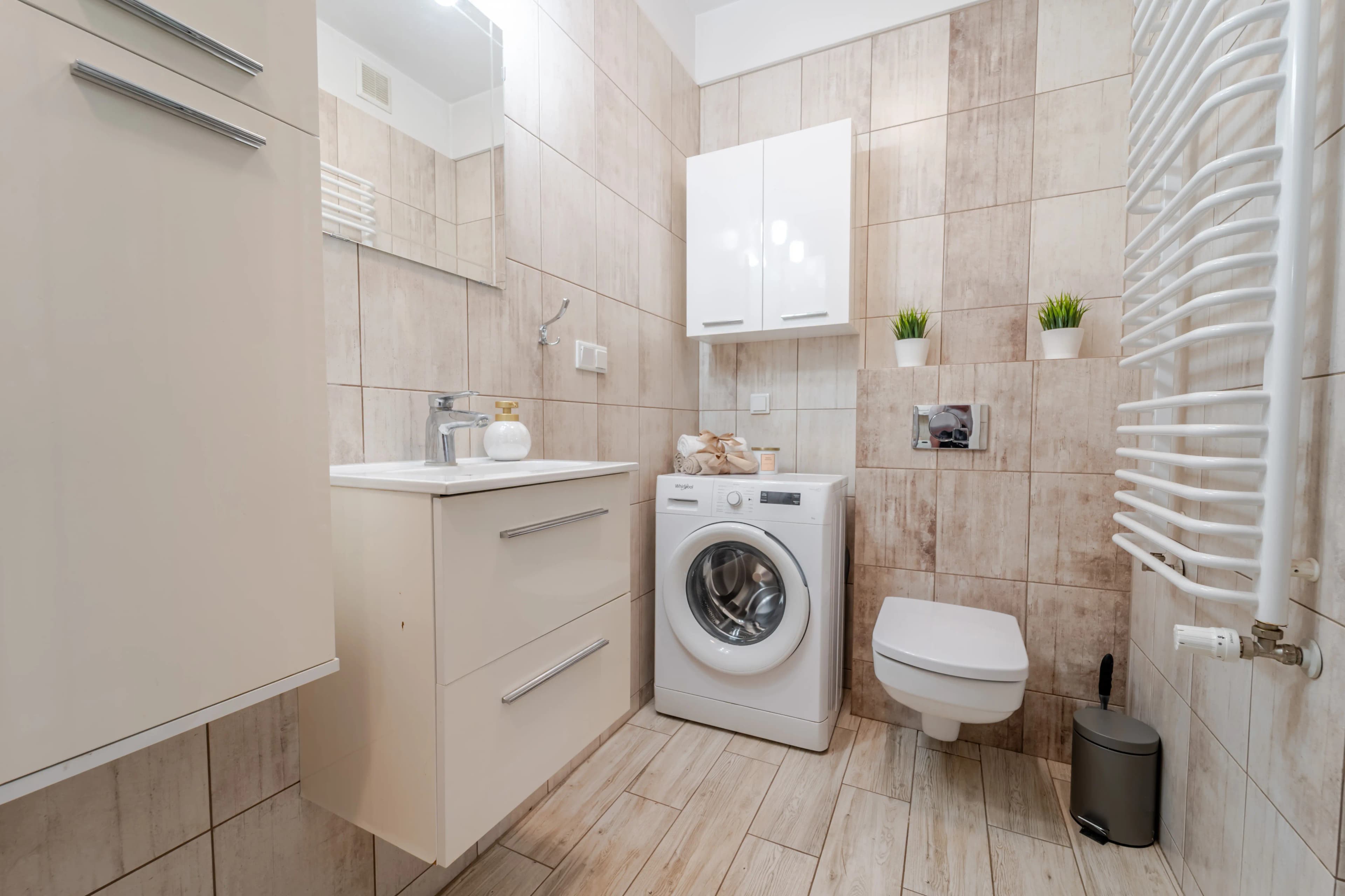 Nowoczesna łazienka w beżowej tonacji z podwieszaną szafką pod umywalkę, dużym lustrem i grzejnikiem drabinkowym.