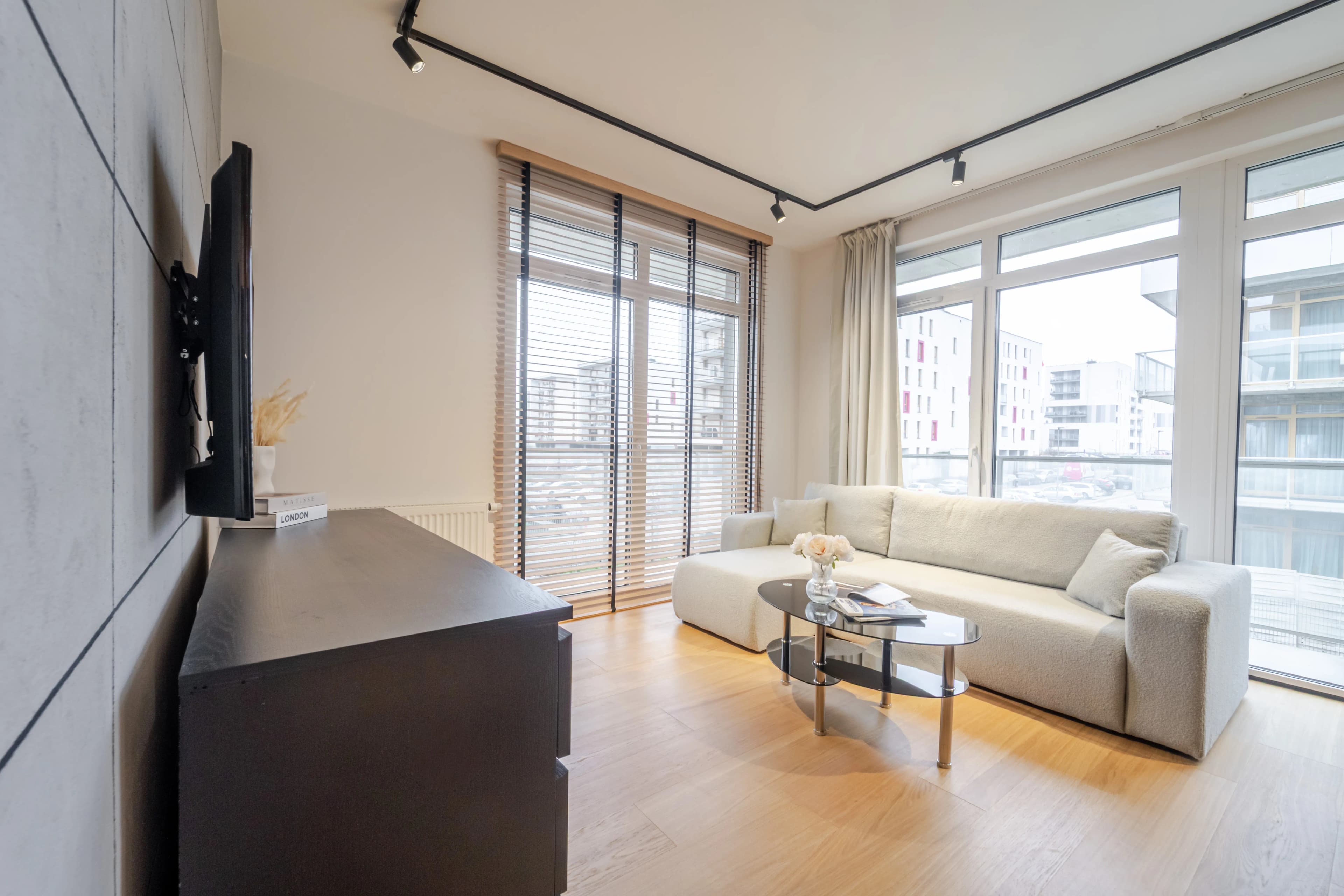 Profesjonalne zdjęcie wnętrza przedstawiające przestronny, jasny salon z aneksem kuchennym i jadalnią, urządzony w eleganckim, nowoczesnym stylu ze złotymi akcentami.