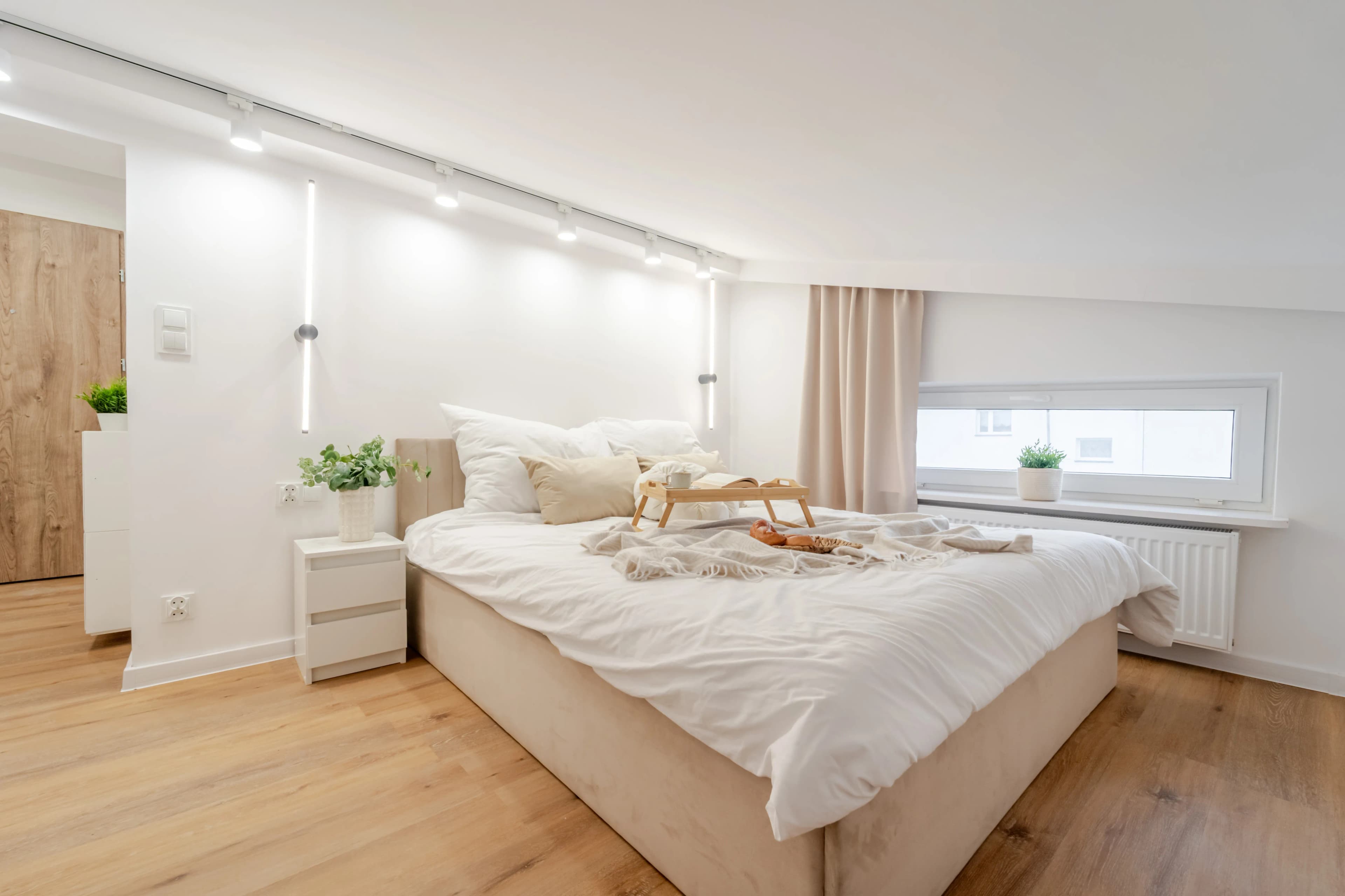 Profesjonalna fotografia wnętrza ukazująca jasny kącik wypoczynkowy z beżową sofą, stolikami kawowymi i dużym oknem z ozdobnymi zasłonami.