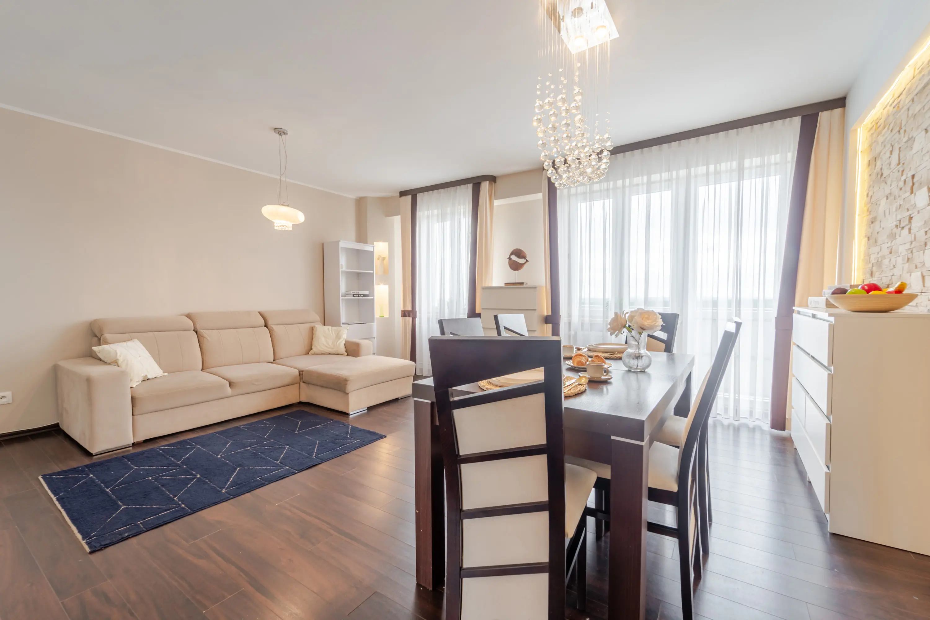 Profesjonalna fotografia jasnej, otwartej przestrzeni dziennej łączącej nowoczesną kuchnię, jadalnię i kącik do pracy w spójnej aranżacji.