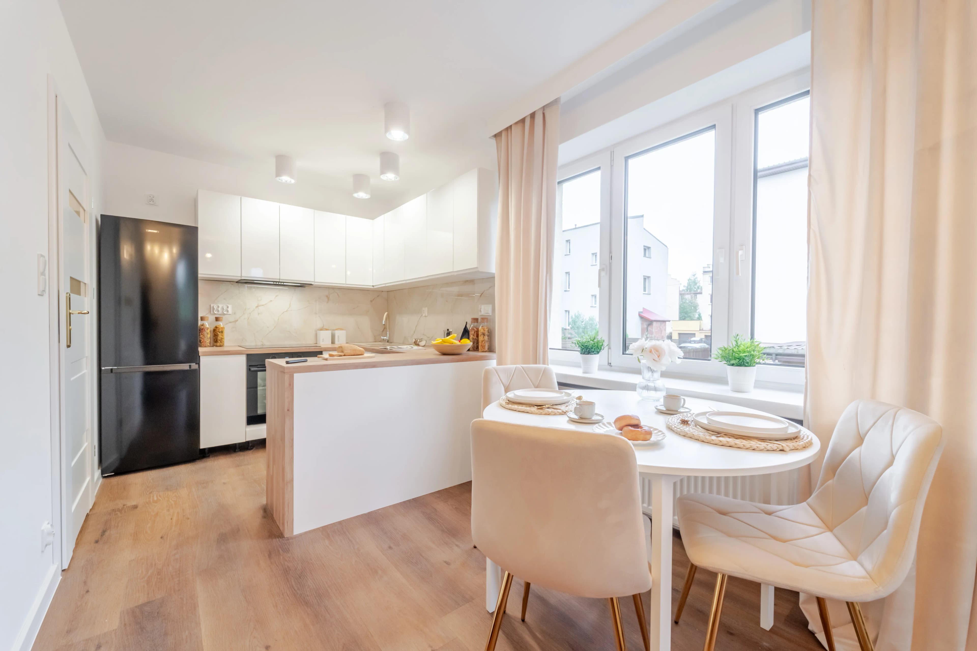 Nowoczesna przestrzeń dzienna łącząca jasny salon z kontrastującym, grafitowo-drewnianym aneksem kuchennym i wyspą z hokerami.