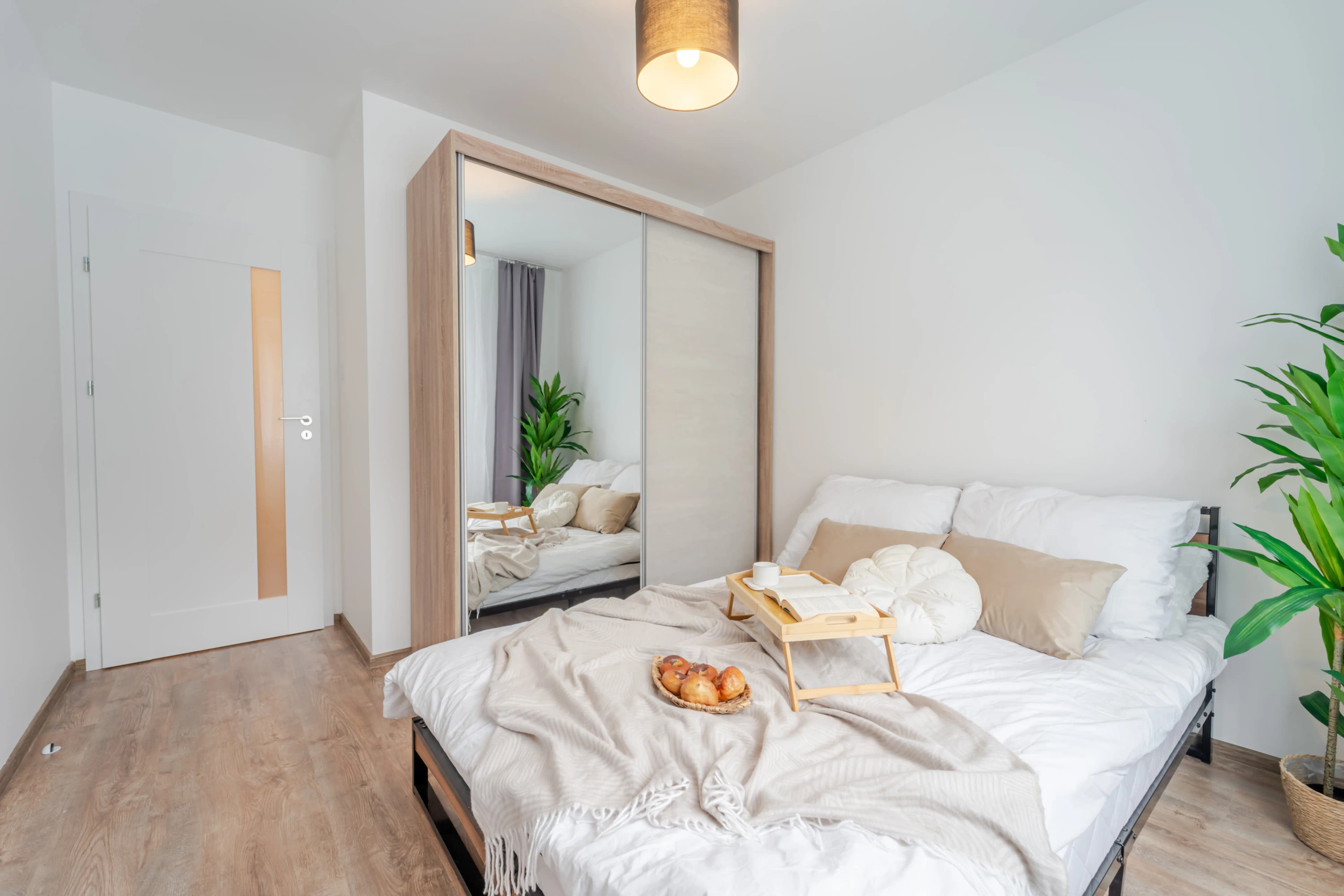 Klimatyczna sypialnia na poddaszu z dużym łóżkiem, nastrojowym oświetleniem liniowym i bielą dominującą w aranżacji.