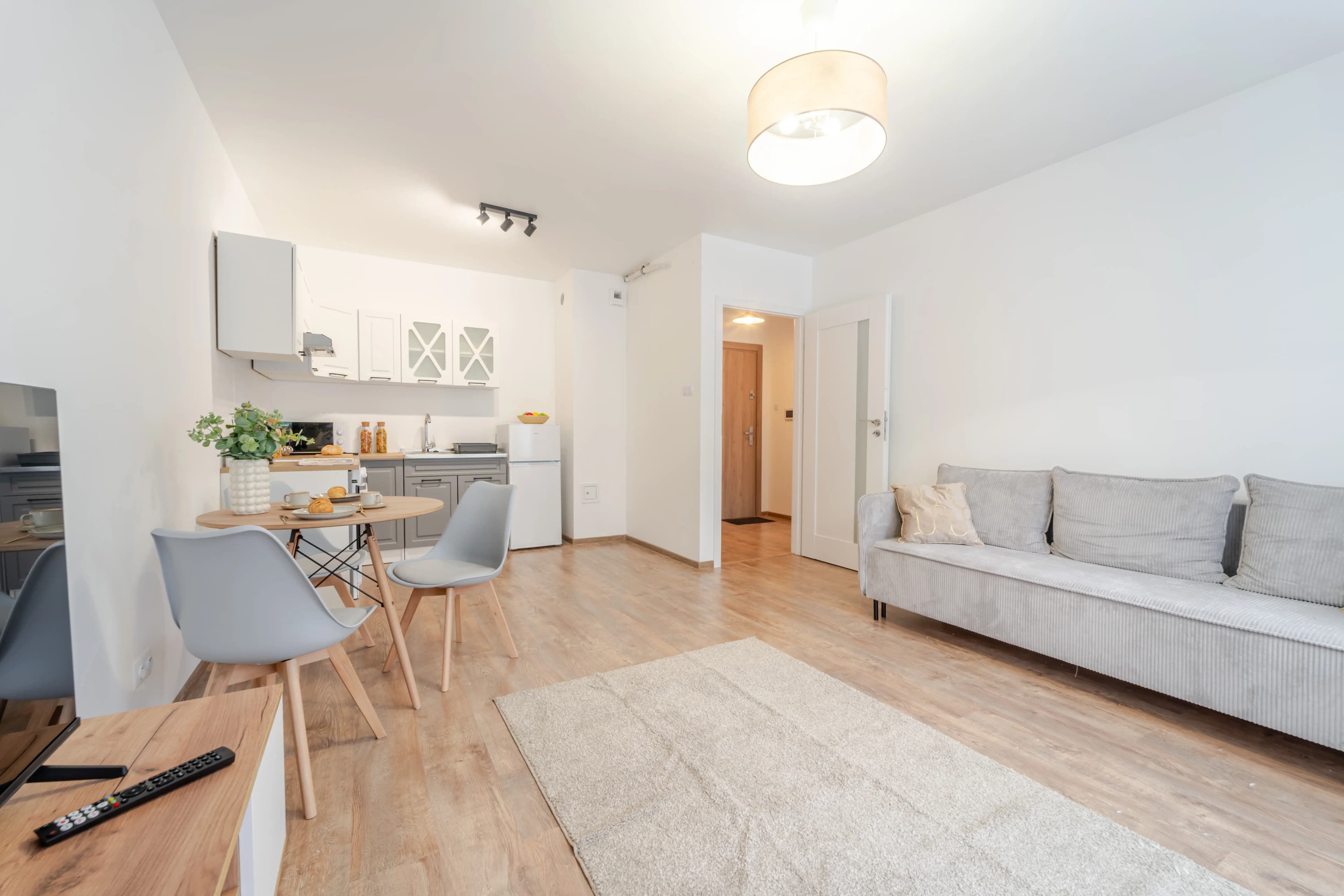 Elegancki salon w stylu glamour z białą sofą, złotymi dodatkami i widokiem na jadalnię w głębi pomieszczenia.