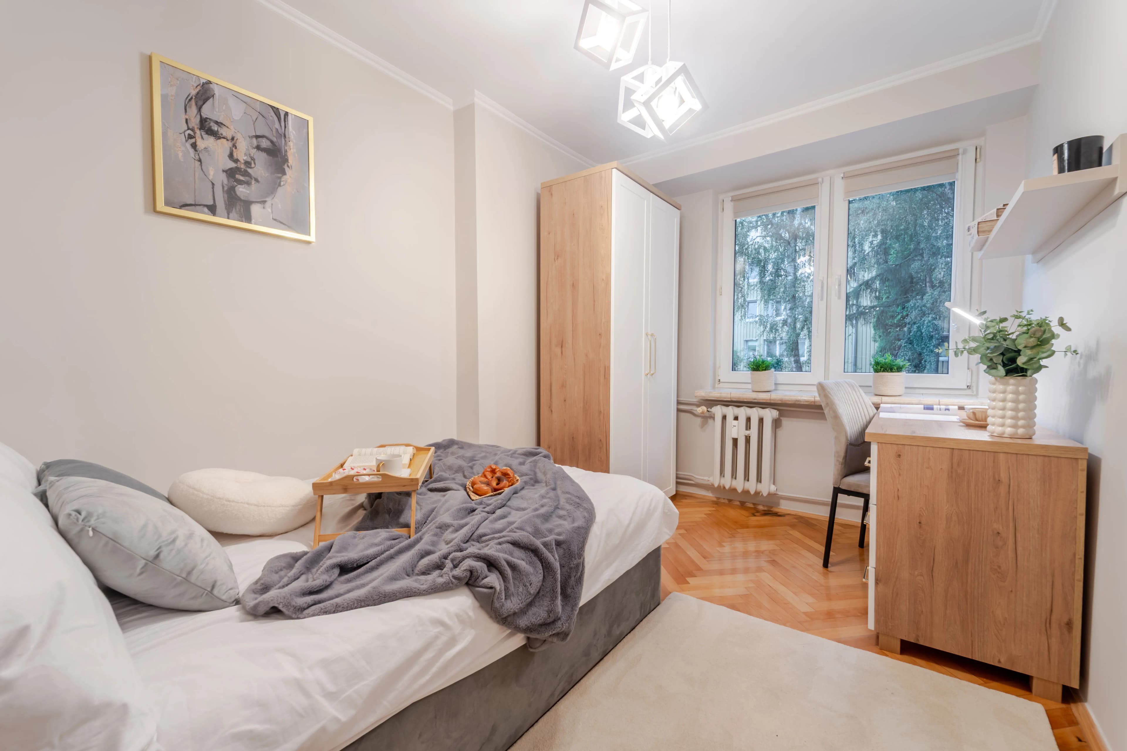 Przestronny, minimalistyczny pokój dzienny z jasną sofą modułową, drewnianym parkietem i otwartą kuchnią w tle.