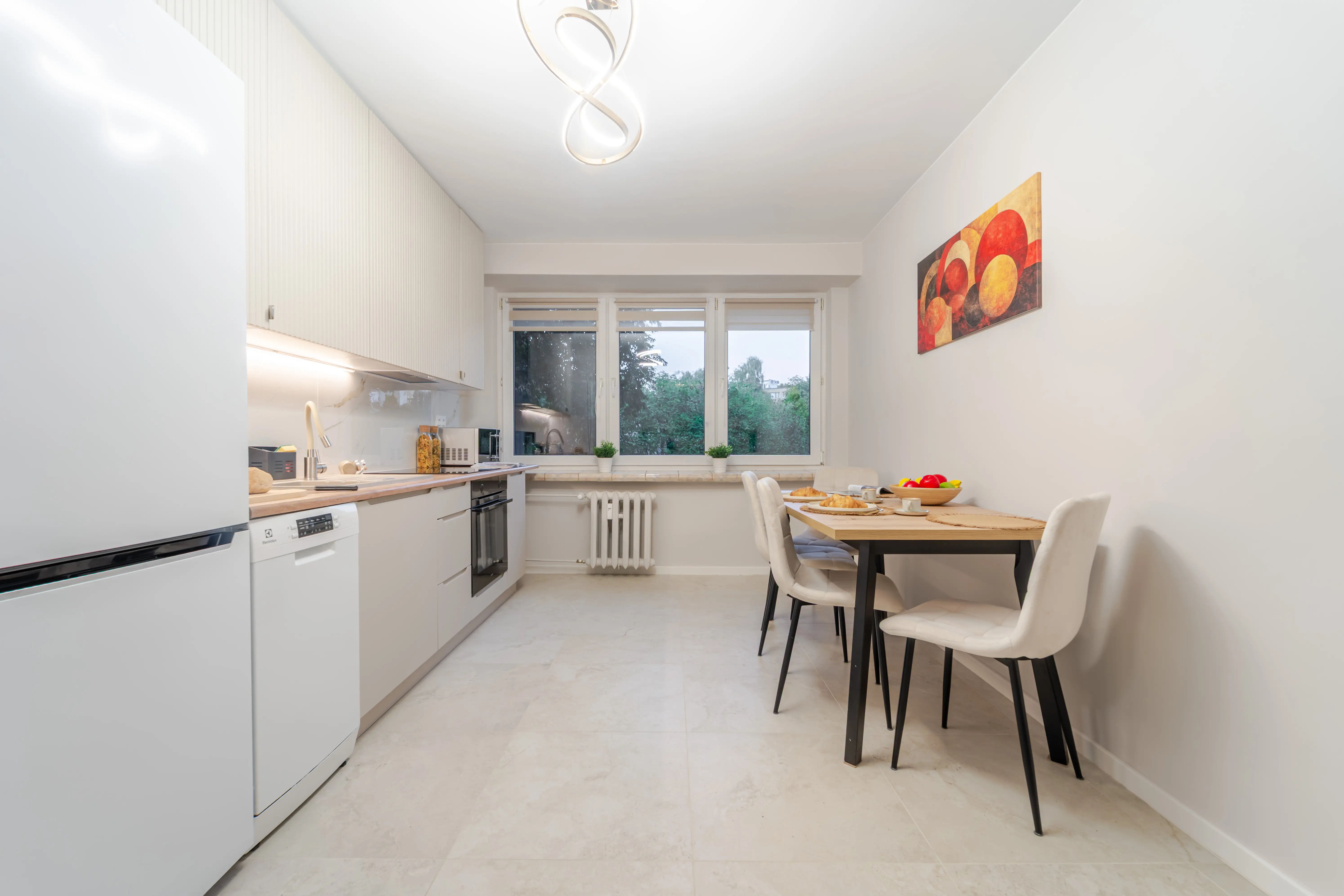 Biała kuchnia w kształcie litery U z kontrastującą czarną lodówką i przytulną strefą jadalnianą przy oknie.