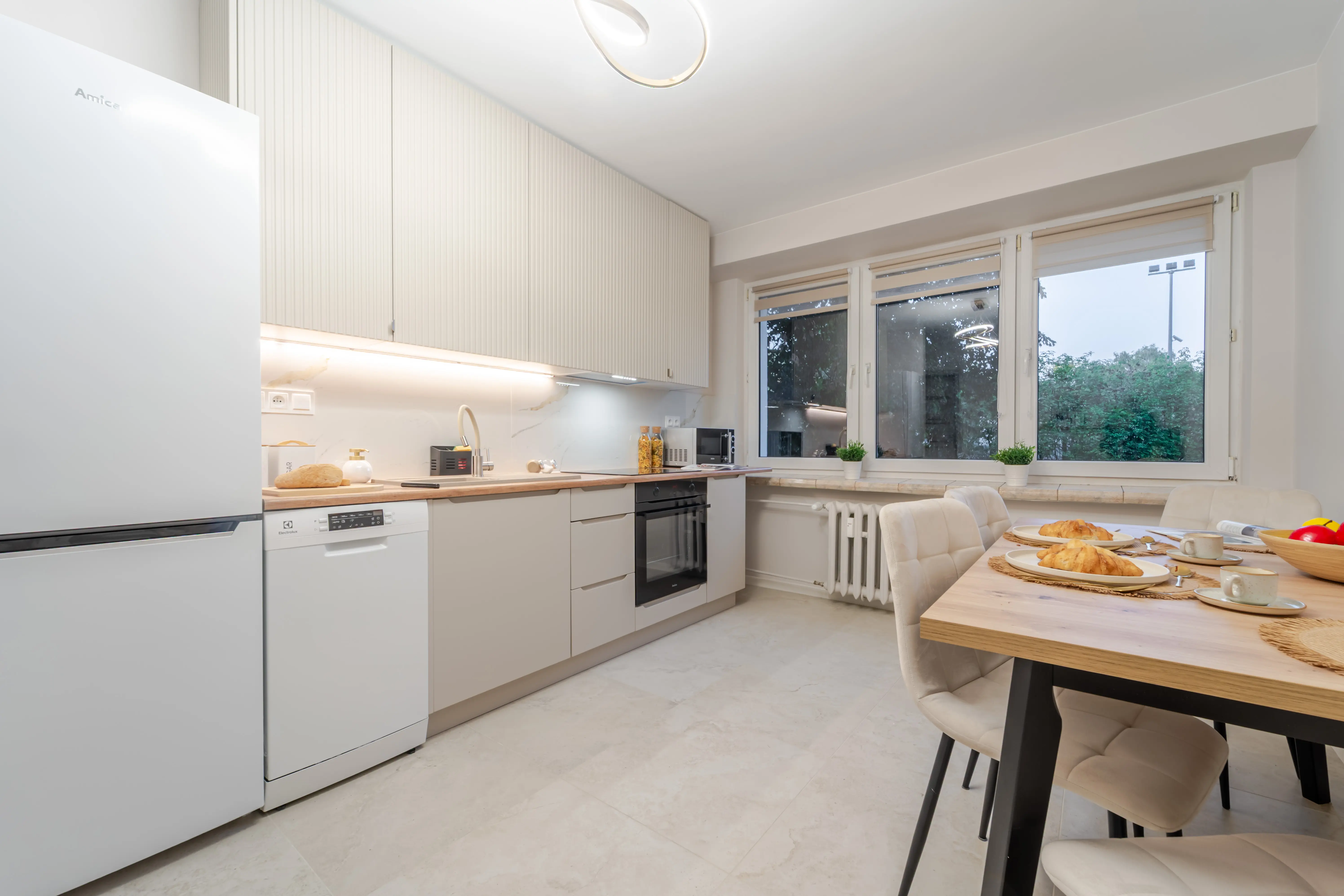 Jasna sypialnia z dużym lustrem na szafie, rośliną doniczkową i łóżkiem przygotowanym do relaksu.