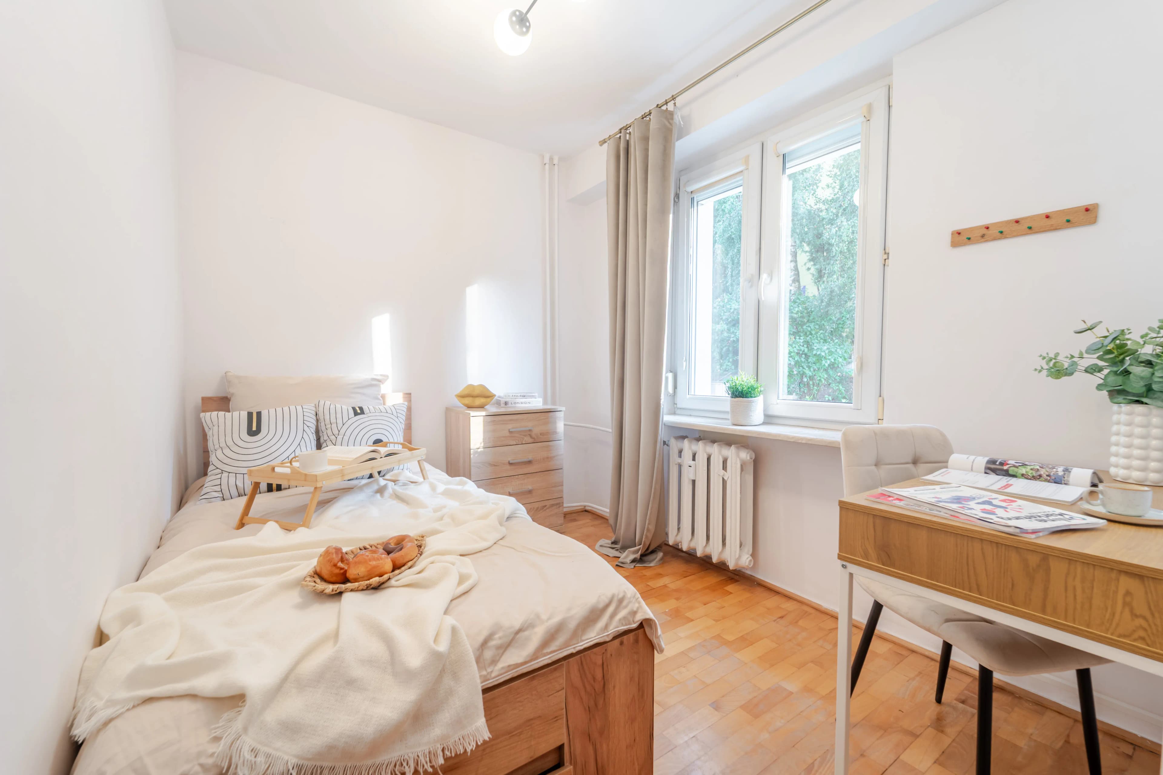 Przytulna sypialnia z miejscem do pracy, udekorowana nowoczesnym obrazem i tacą śniadaniową na łóżku.