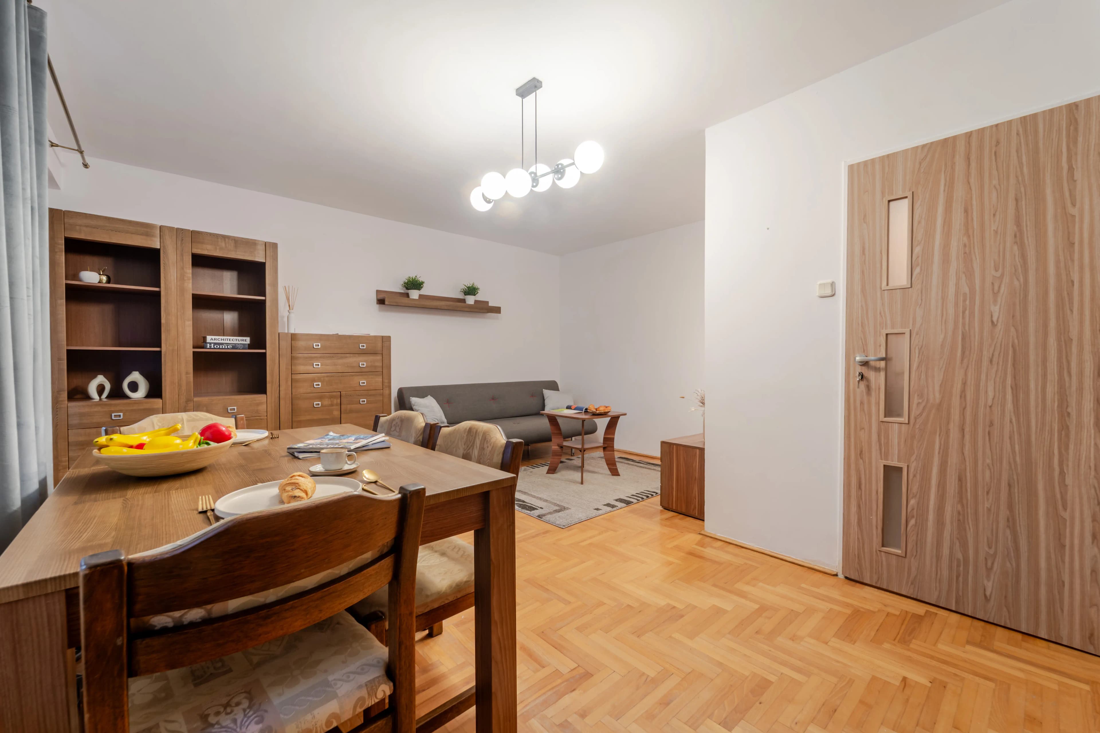 Przestronna kuchnia z jasną zabudową, dużym oknem i stołem jadalnianym ożywiona kolorowym akcentem w postaci obrazu na ścianie.