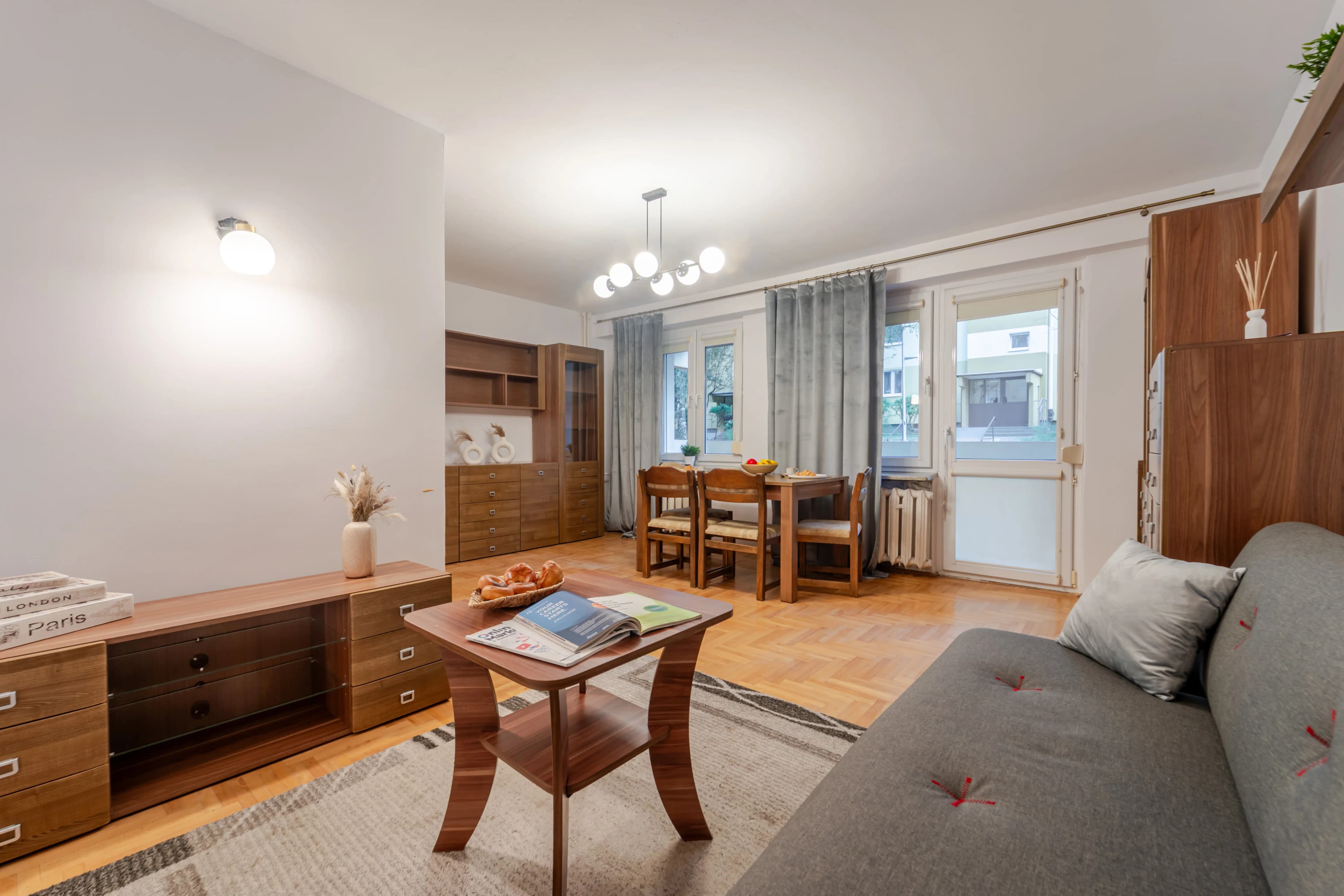 Nowoczesna kuchnia z modnymi, ryflowanymi frontami szafek wiszących i dużym, drewnianym stołem na pierwszym planie.