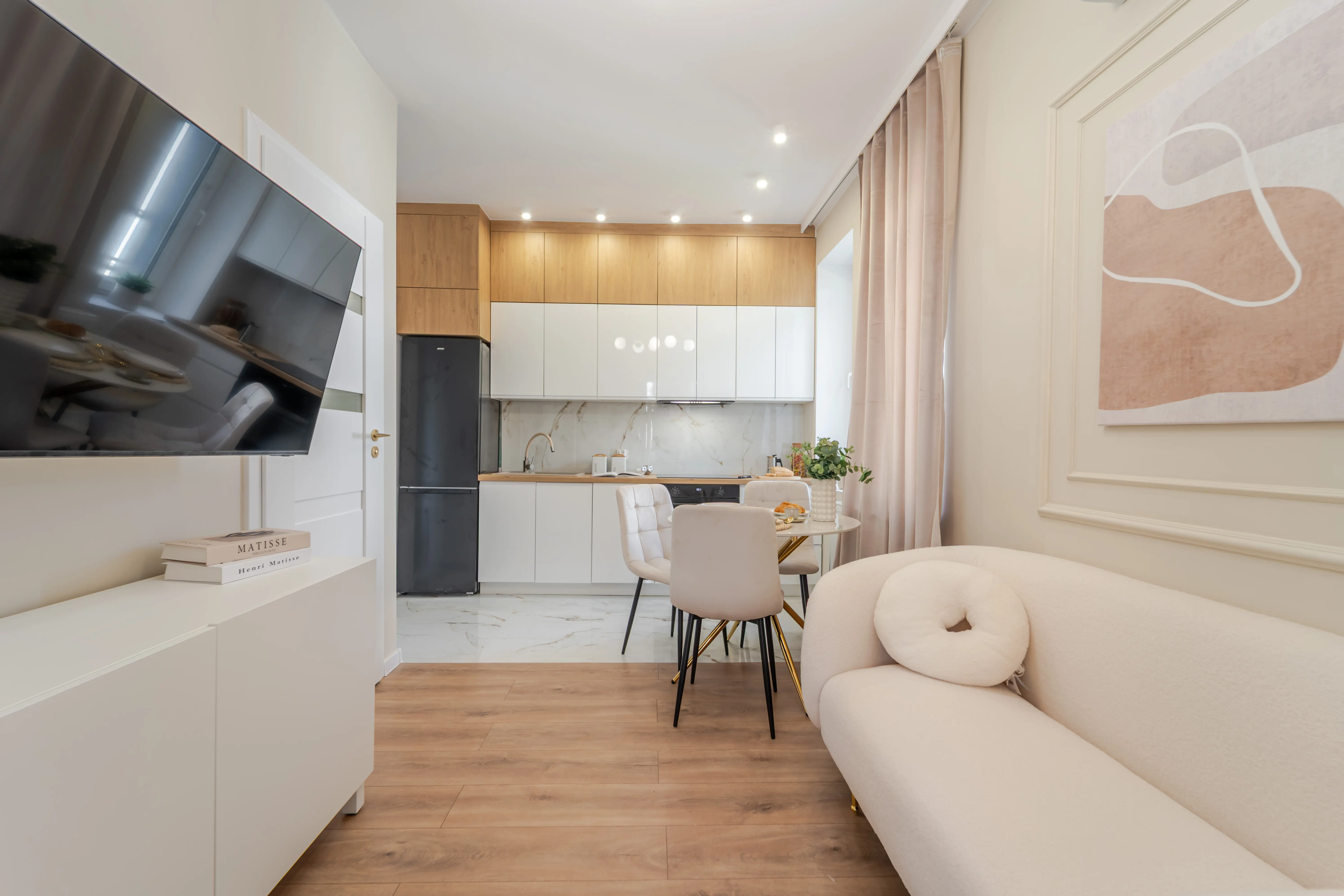 Elegancka, biała sypialnia z toaletką, złotymi kinkietami i dużym balkonem wpuszczającym do wnętrza naturalne światło.