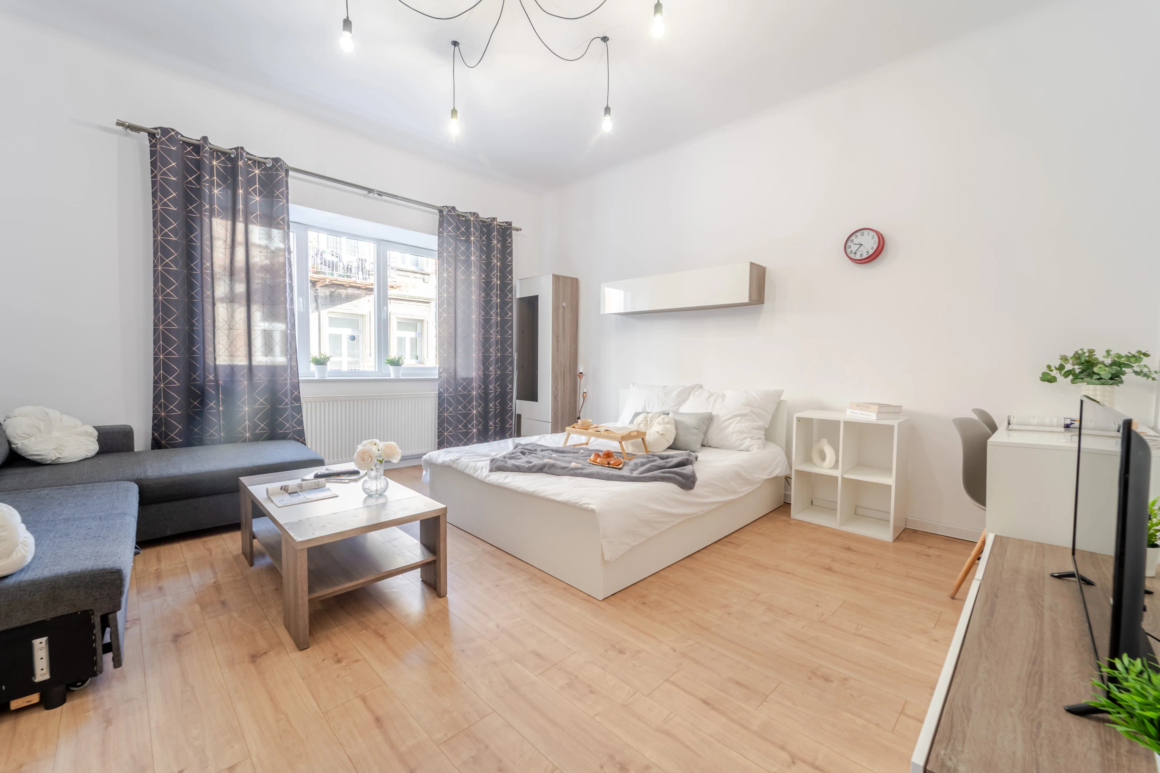 Luksusowy apartament z jasną, zaokrągloną sofą, wiszącym telewizorem i widokiem na nowoczesny aneks kuchenny w tle.